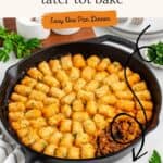 Skillet with sloppy joe tater tot bake, golden tots on top, garnished with herbs, beside napkin and utensils.