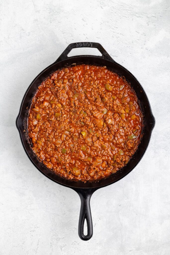 Black cast iron skillet with ground meat and tomato sauce mixture, top-down view on light surface.