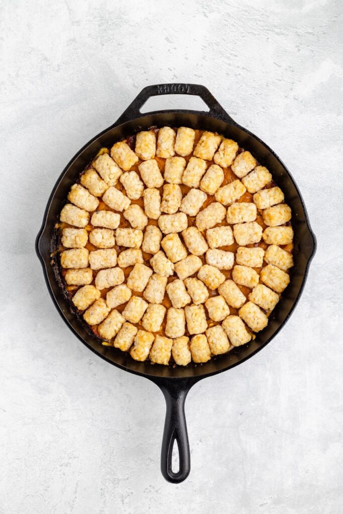 Cast iron skillet with tater tots arranged in a circular pattern on a light background.