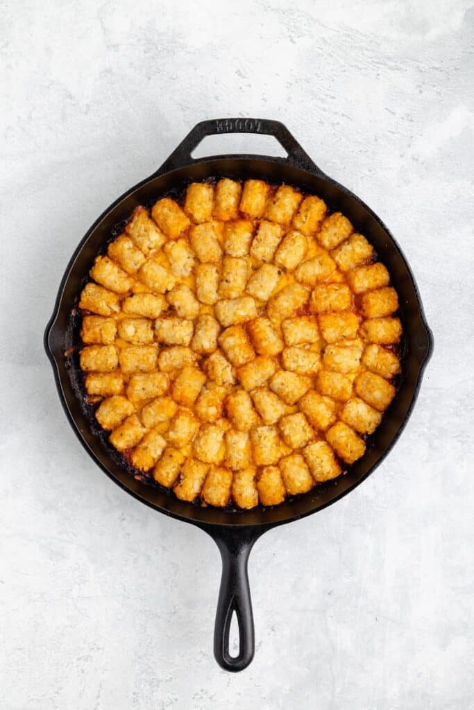 Cast iron skillet filled with golden-brown tater tots, neatly arranged on a light gray background surface.
