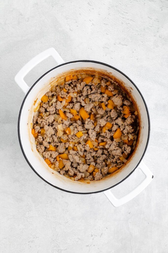 White pot with cooked ground meat, yellow bell peppers, and onions on a light gray surface.