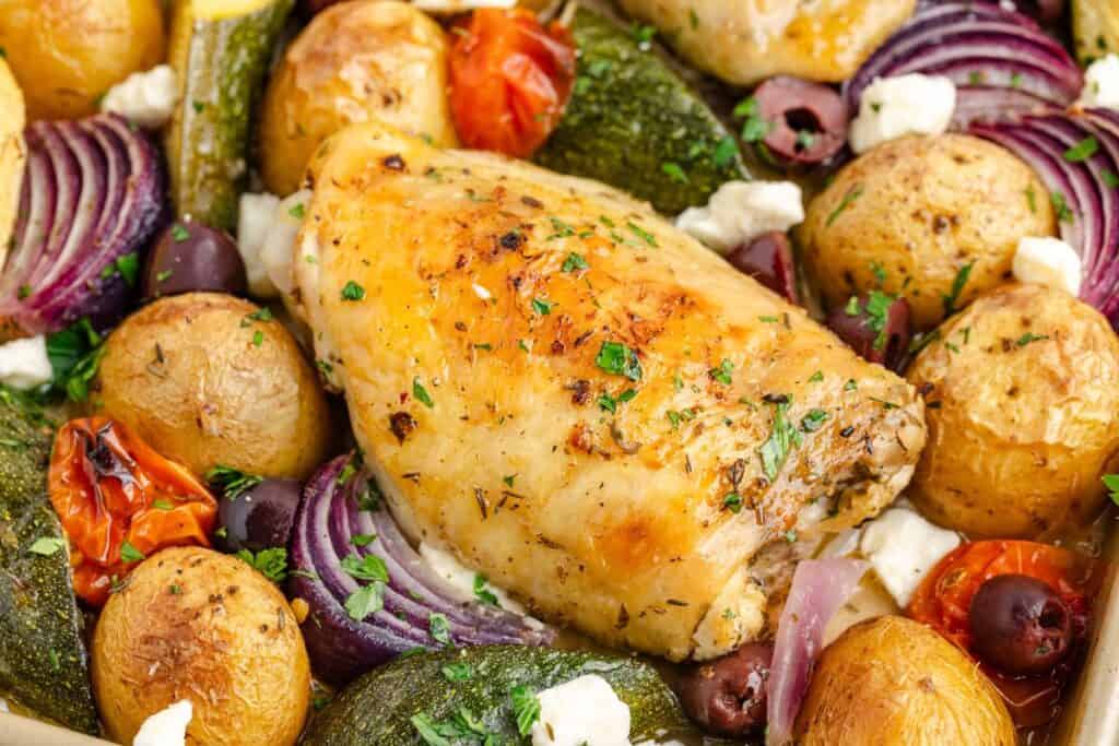 Greek sheet pan chicken  with baby potatoes, red onions, tomatoes, olives, zucchini, feta cheese, and fresh herbs.