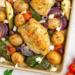 Sheet pan Greek chicken, roasted vegetables, olives, and feta cheese, topped with fresh herbs.
