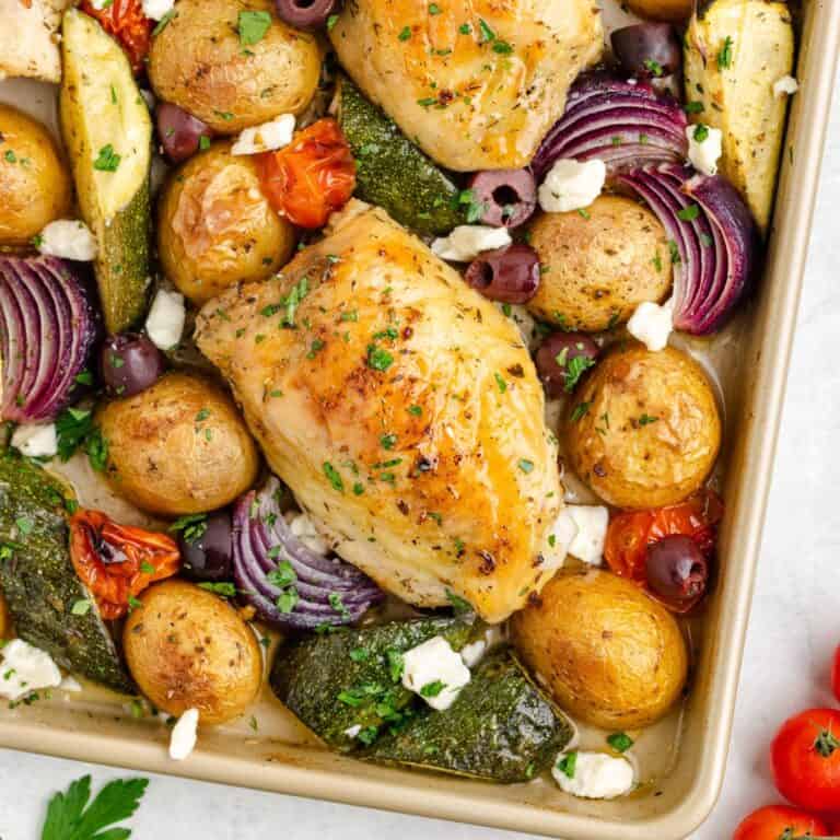 Sheet pan Greek chicken, roasted vegetables, olives, and feta cheese, topped with fresh herbs.