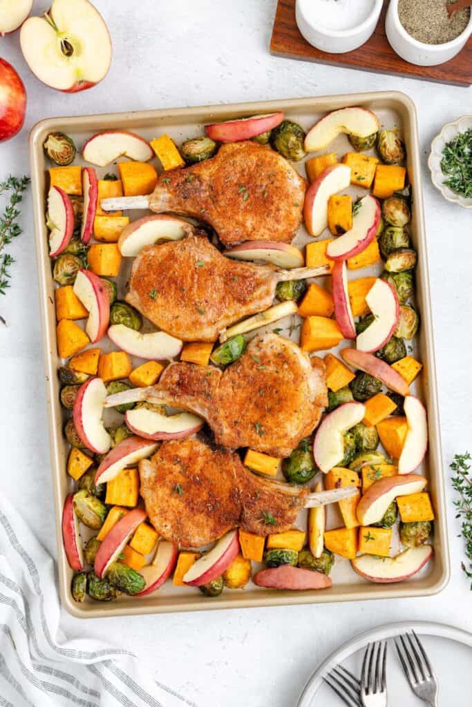 Sheet pan pork chops and apples, Brussels sprouts, squash, and onions arranged for roasting.