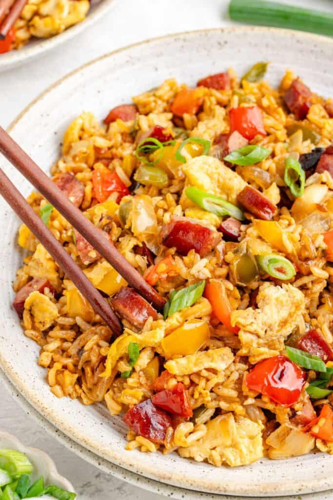 Fried rice with sausage and peppers, and green onions; chopsticks rest beside the bowl.