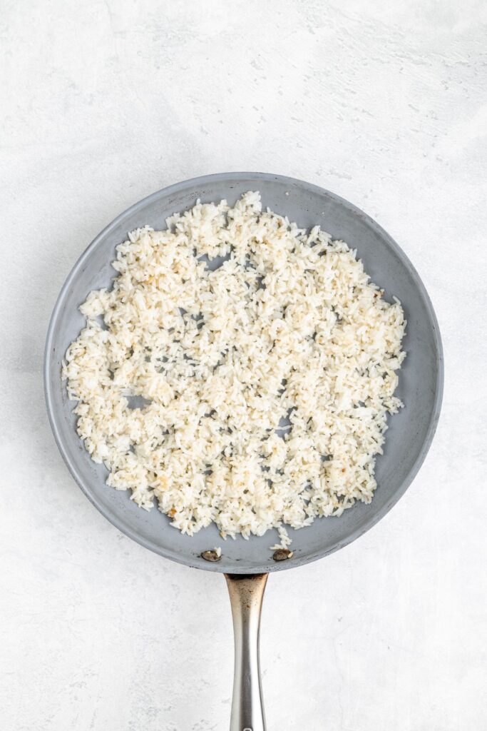 Frying pan with evenly spread cooked white rice on a light countertop.