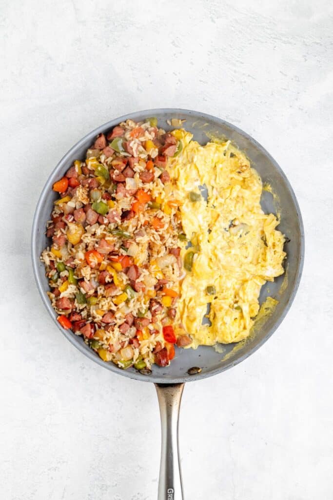A skillet with scrambled eggs on one side and diced vegetables, sausage, and rice on the other.