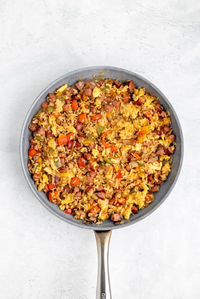 Frying pan with fried rice, vegetables, eggs, and meat pieces on a light surface.