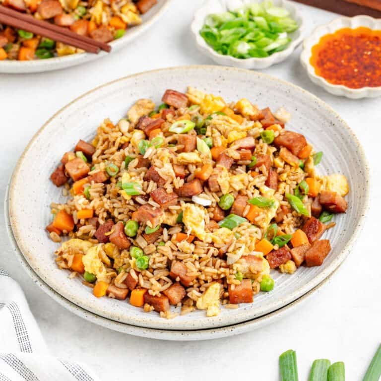 Spam fried rice with eggs, peas, carrots, green onions on a plate; sauces and sliced green onions on the side.