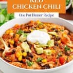 Bowl of red chicken chili with avocado, sour cream, and vegetable garnish.