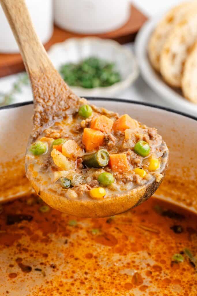 Wooden ladle holding cottage pie soup above a pot.