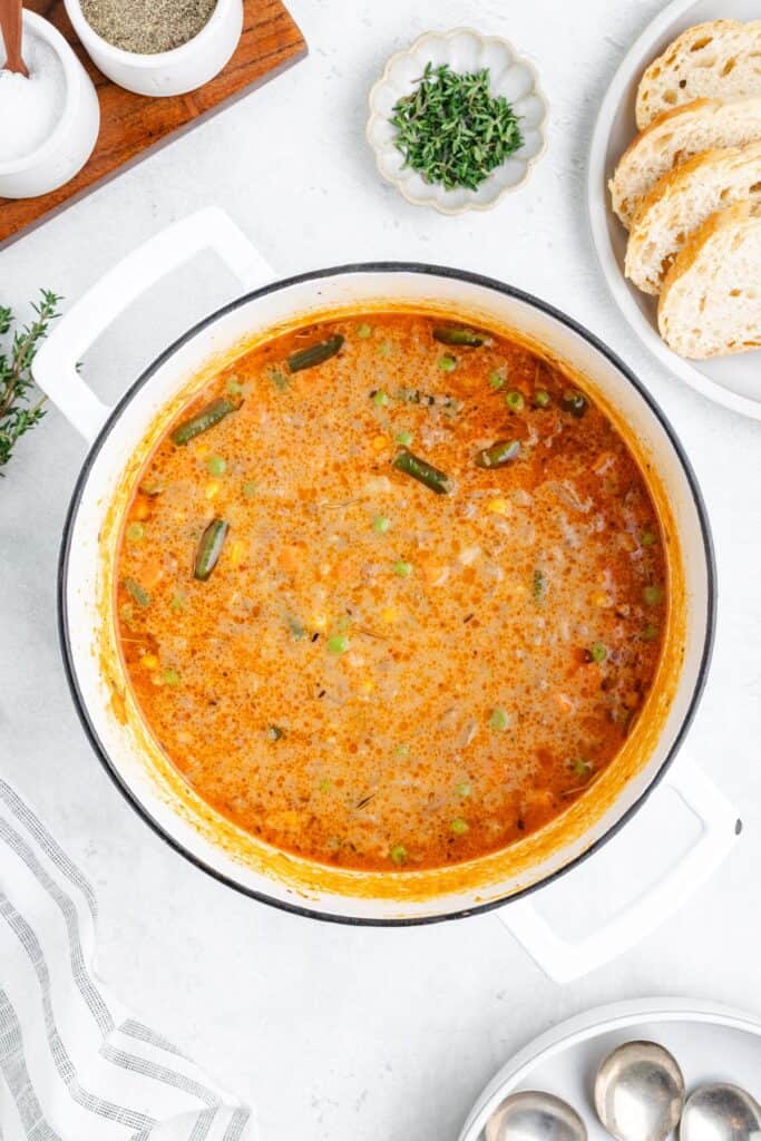 Pot of shepherd's pie soup with green beans and peas, surrounded by bread, herbs, and a striped napkin.