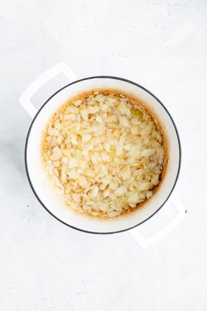 Chopped onions sautéing with browning in a white pot on a light surface.