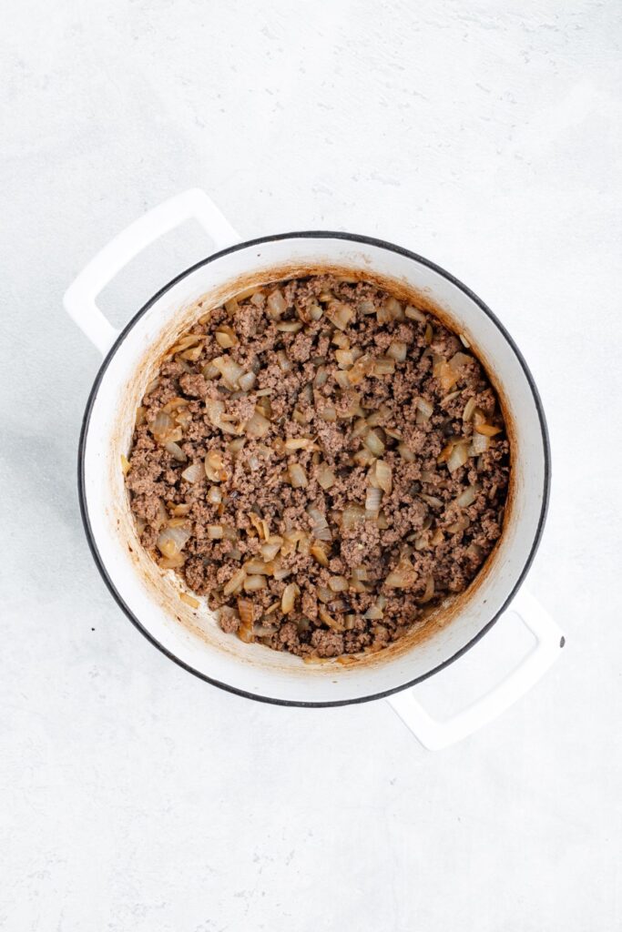Cooked ground beef with diced onions in a white pot, seen from above on a light surface.
