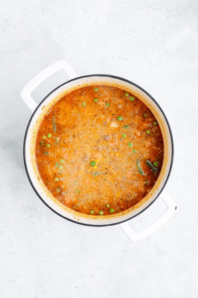 White pot with reddish-brown stew and green peas, viewed from above on a light-colored surface.