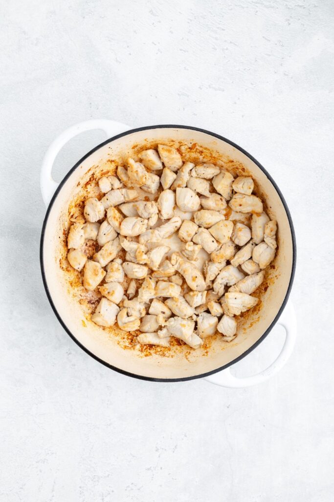 Diced, cooked chicken in a white Dutch oven on a light surface.