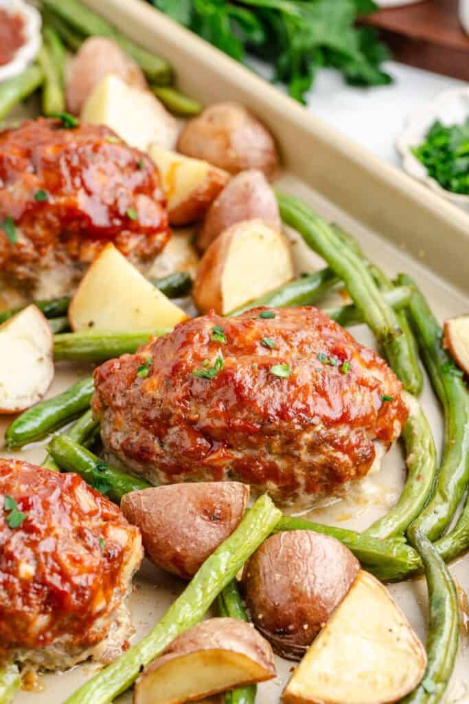 Sheet pan of glazed mini meatloaves with roasted green beans and potatoes.