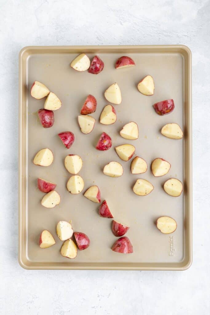 Halved red potatoes arranged on a light baking sheet, prepared for roasting.