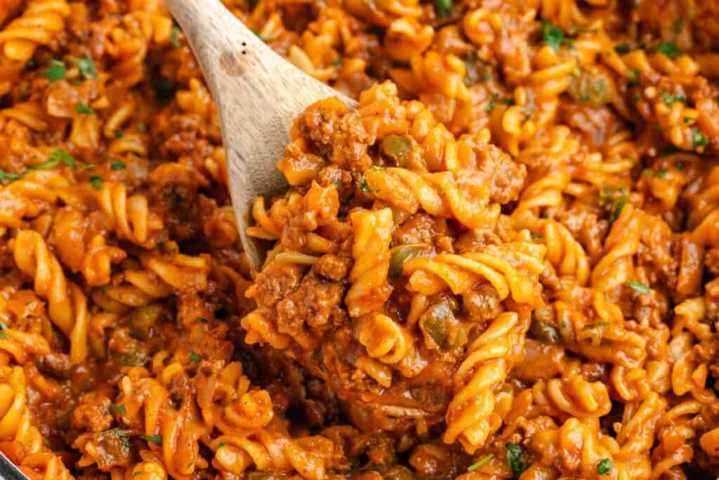 Wooden spoon lifting sloppy joes pasta with ground meat, tomato sauce, and herbs.