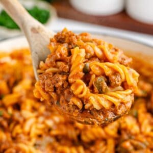 Wooden spoon lifts sloppy joe pasta with ground beef and tomato sauce above a pot of the same meal.