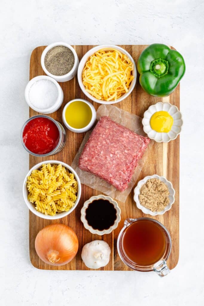 Sloppy Joe Pasta ingredients like ground beef, cheese, bell pepper, pasta, tomato sauce on a wooden board.