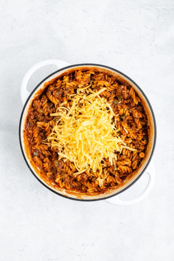 White pot holding rotini pasta in meat sauce, topped with shredded cheese.