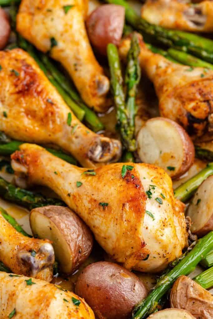 Baked chicken drumsticks with roasted red potatoes and asparagus, topped with chopped fresh herbs.