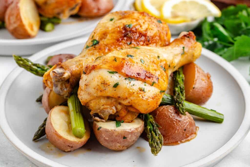 Roasted chicken legs with red potatoes and asparagus, garnished with herbs on a plate.