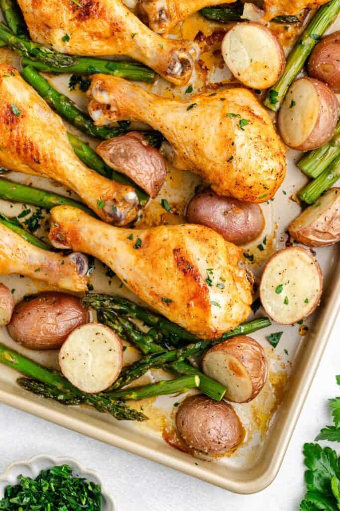Sheet pan chicken drumsticks, with red potatoes, asparagus, and chopped herb garnish.