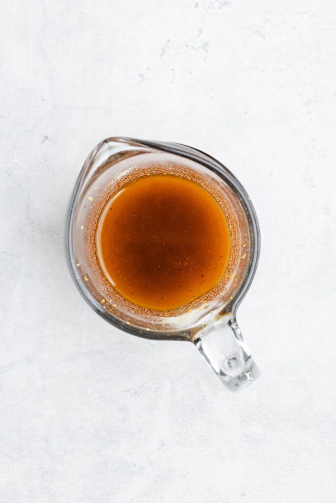 Glass measuring cup with brown liquid, viewed from above on a light gray background.