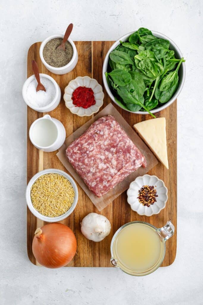 Wooden board with raw ground meat, spinach, cheese, orzo, garlic, onion, broth, spices, tomato paste, and milk.