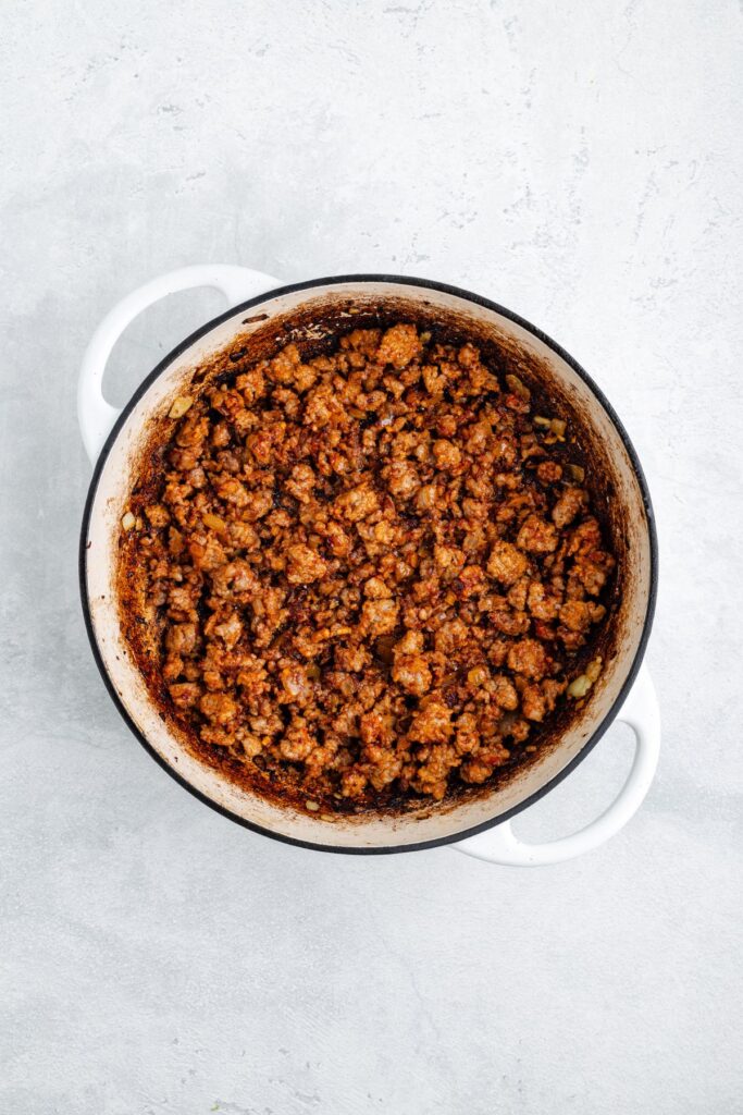 White pot containing cooked, browned ground meat with spices on a light gray surface.