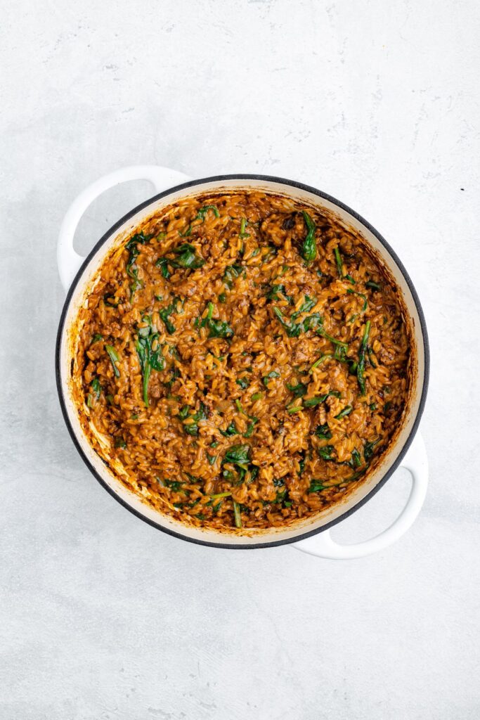White pot of cooked rice with greens and reddish-brown sauce on a light gray surface.