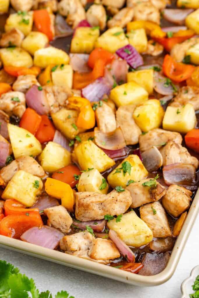Hawaiian sheet pan chicken with pineapple, red onions, and bell peppers topped with fresh herbs.