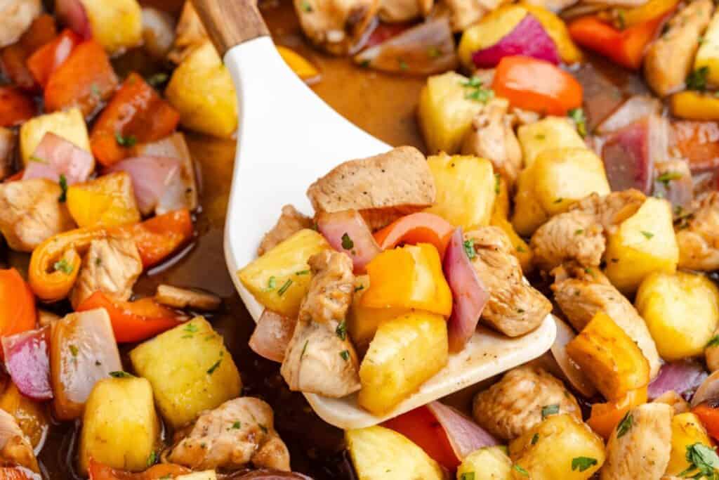A white spatula lifts Pineapple Chicken Sheet Pan.