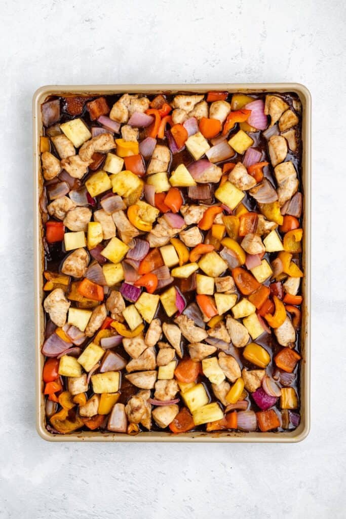 Sheet pan with roasted chopped chicken, pineapple, red onion, and bell peppers on a light background.