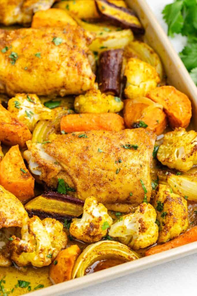 Baked Moroccan chicken thighs and roasted vegetables, including cauliflower, carrots, onions, and sweet potatoes in a baking dish.