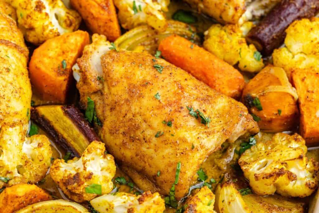 Moroccan sheet pan chicken with cauliflower, sweet potato, carrot, and onion on a baking tray.