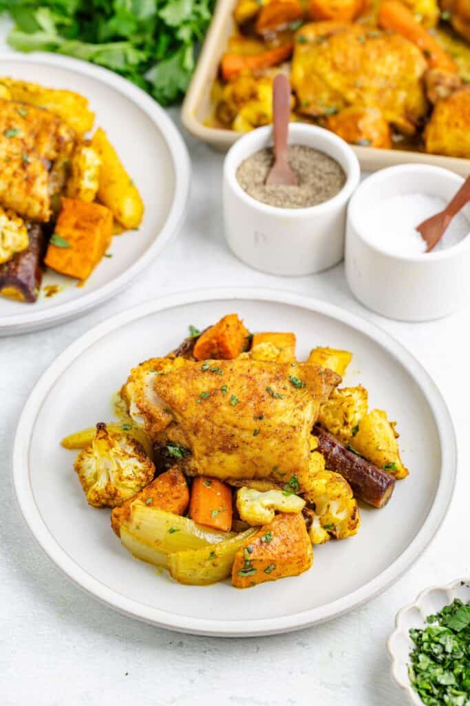 Sheet pan Moroccan chicken with carrots, cauliflower, and sweet potatoes on a plate, garnished with herbs.