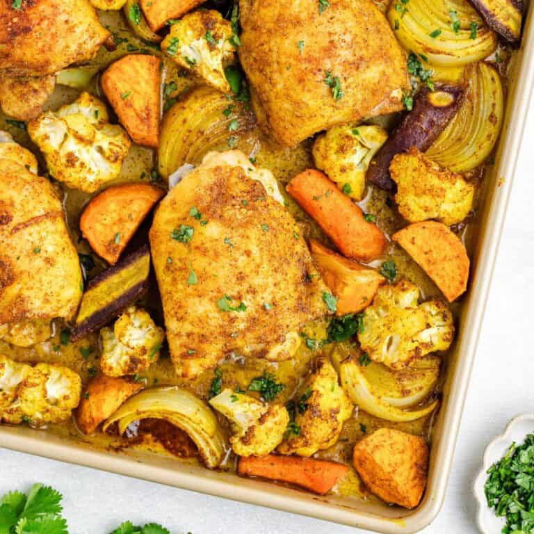 Sheet pan Moroccan chicken with sweet potatoes, carrots, onions, cauliflower, and herbs.