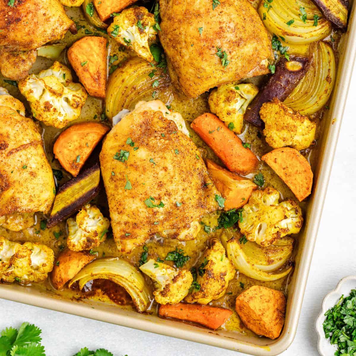 Sheet pan Moroccan chicken with sweet potatoes, carrots, onions, cauliflower, and herbs.