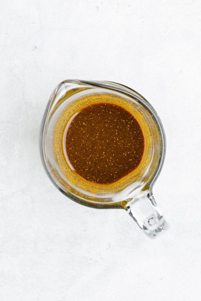 A glass measuring cup with dark brown sauce sits on a light gray surface.