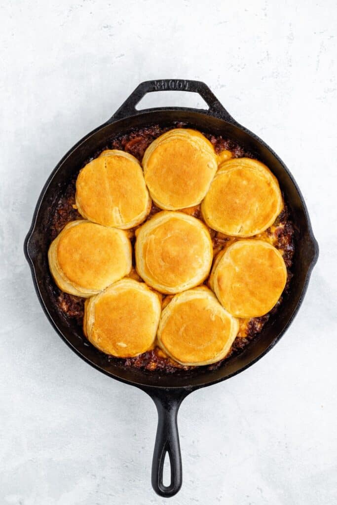 Baked biscuits in a cast iron skillet, arranged in a circle atop savory filling, seen from above.