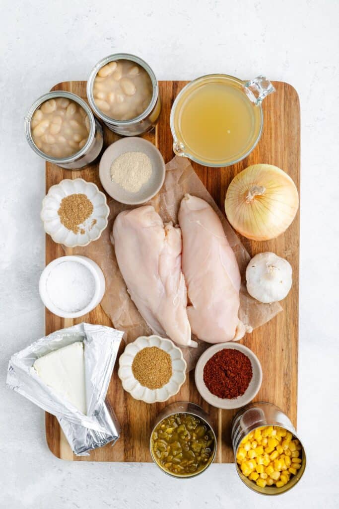 Chicken, beans, broth, onion, garlic, cream cheese, green chilies, corn, and spices on a wooden board.