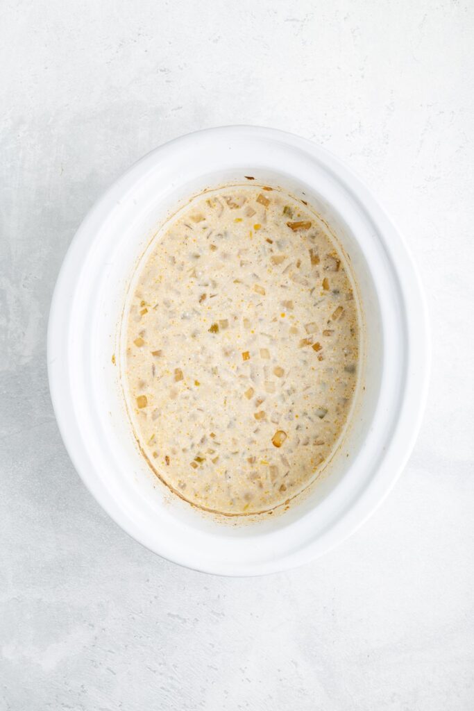 White slow cooker with creamy vegetable soup, seen from above on a light surface.