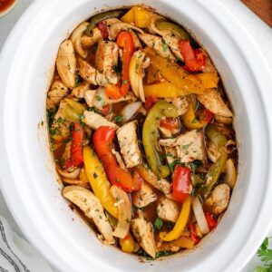 Crockpot chicken fajitas with herbs in a white slow cooker.