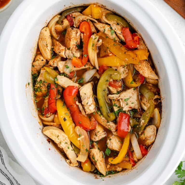 Crockpot chicken fajitas with herbs in a white slow cooker.