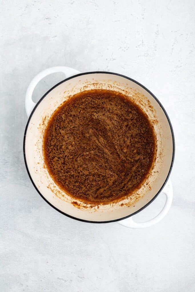A white Dutch oven filled with a dark brown, liquid sauce.
