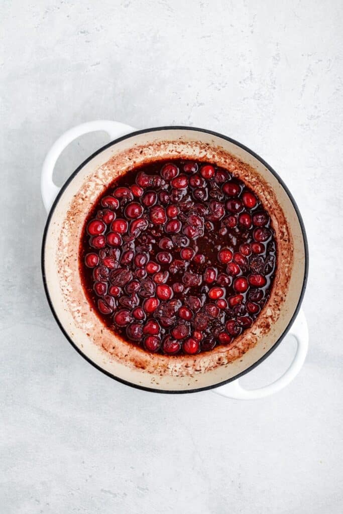 A white pot filled with cooked, dark red cranberries in sauce.